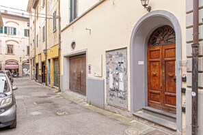 A narrow street with buildings, a parked car, and a closed shop with a shutter.