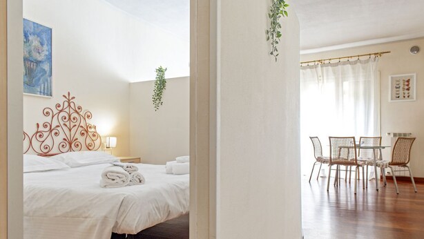 Una camera d'albergo con un letto, un tavolo e sedie, e una finestra con tende.