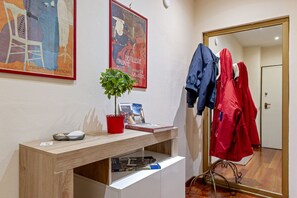 A room with a wooden desk, a potted plant, a mirror, and a coat rack with red jackets.