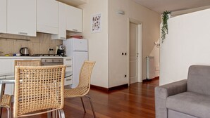 Una cucina moderna con mobili bianchi, un'area pranzo con sedie in vimini e un divano grigio in un soggiorno.