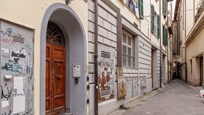 Un vicolo stretto con una porta in legno e un cancello metallico, circondato da edifici con graffiti e un armadietto utenze.
