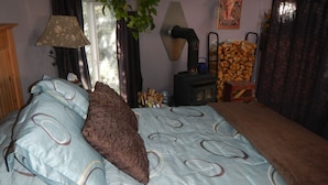 Quarto com cama, janela com cortinas, planta, lareira e cadeira com lenha.