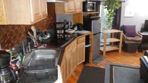 Cozinha compacta com armários de madeira, pia de aço inoxidável, micro-ondas e geladeira.