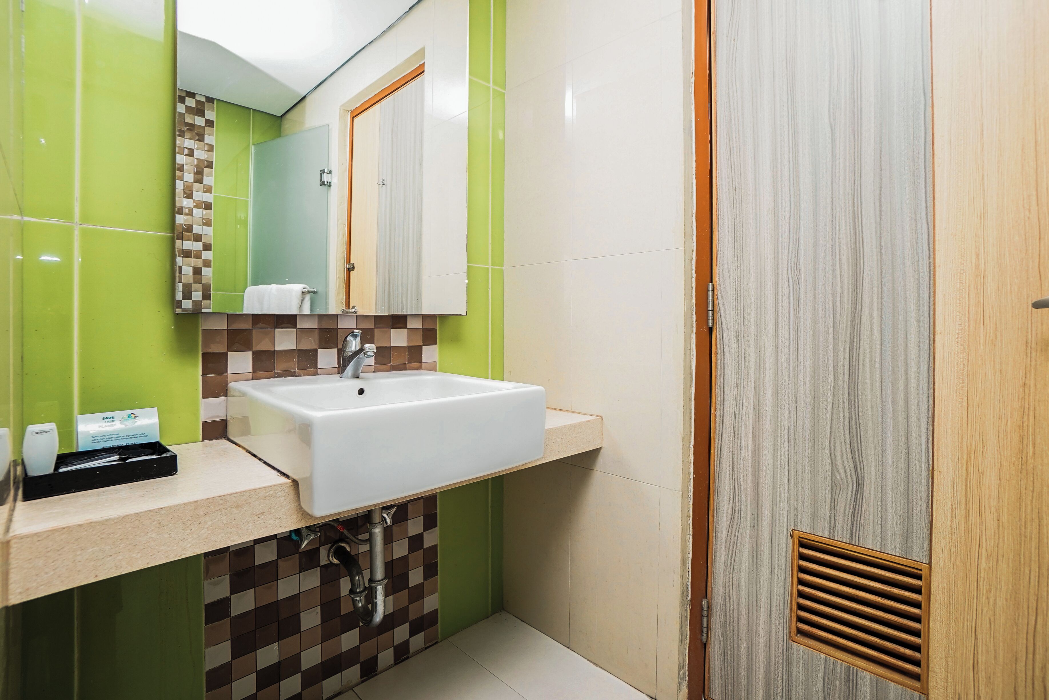 Un baño con un lavamanos blanco, baldosas a cuadros verdes y marrones, un espejo y una puerta de madera.