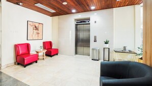 A lobby with a wooden ceiling, two red chairs, a black chair, a small table with a plant, and an elevator. - UTC Dago Hotel Bandung (Bandung)