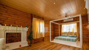 A cozy room with wooden walls, a fireplace, a bed with a checkered bedspread, and a small Christmas tree. - Villa 107 Amarja's Citadel Nest (Mawal)