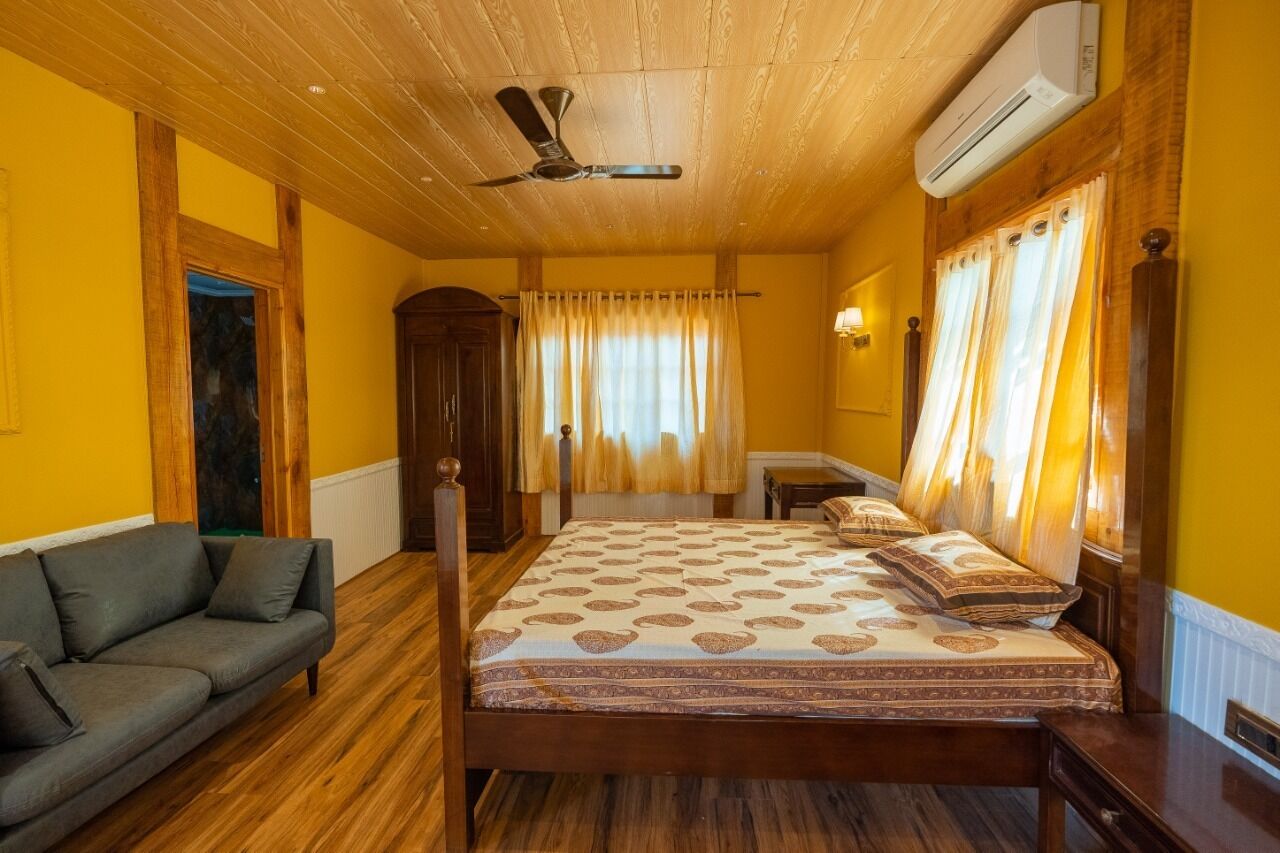 A room with a wooden ceiling, a bed with patterned bedding, a sofa, and curtains on the windows.