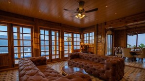 A spacious room with a large sectional sofa, a dining area, and large windows offering a view of the mountains. - Villa 107 Amarja's Citadel Nest (Mawal)
