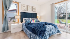 Ein Schlafzimmer mit einem großen Bett, einem Deckenventilator, einem Fenster mit Vorhängen und Blick ins Freie.