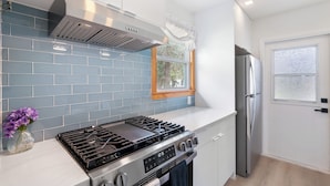 Eine moderne Küche mit Gasherd, Edelstahlgeräten und einer blau gefliesten Spritzschutzwand.