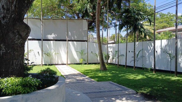 A paved pathway leading to a white building with a low fence and small trees. - Lanka Global  (Jaffna)