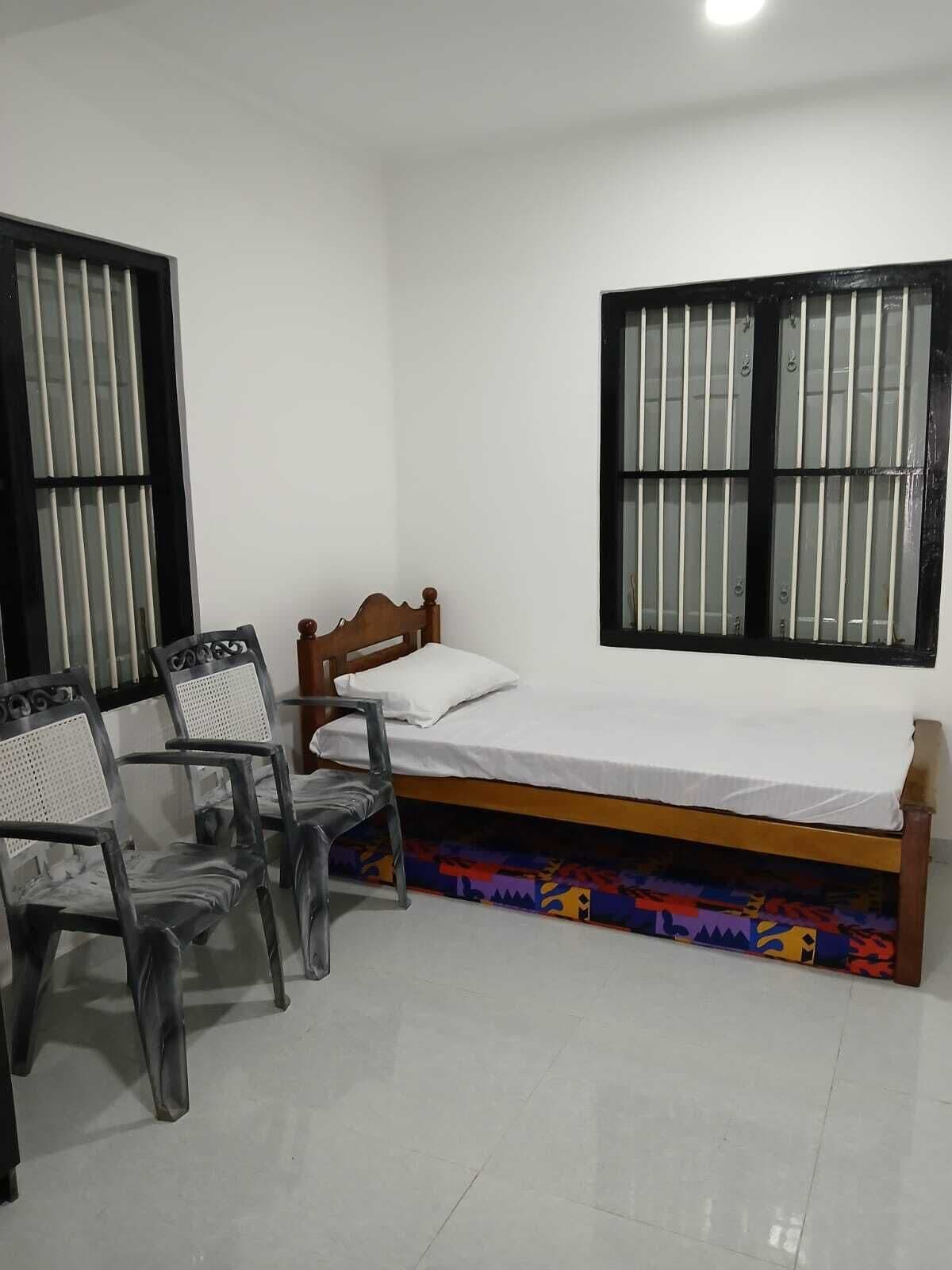 A small, clean room with a single bed, two chairs, and a window with bars.