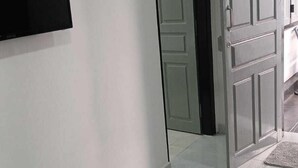 A hallway with a tiled floor, a closed door, and a flat-screen TV mounted on the wall. - Lanka Global  (Jaffna)