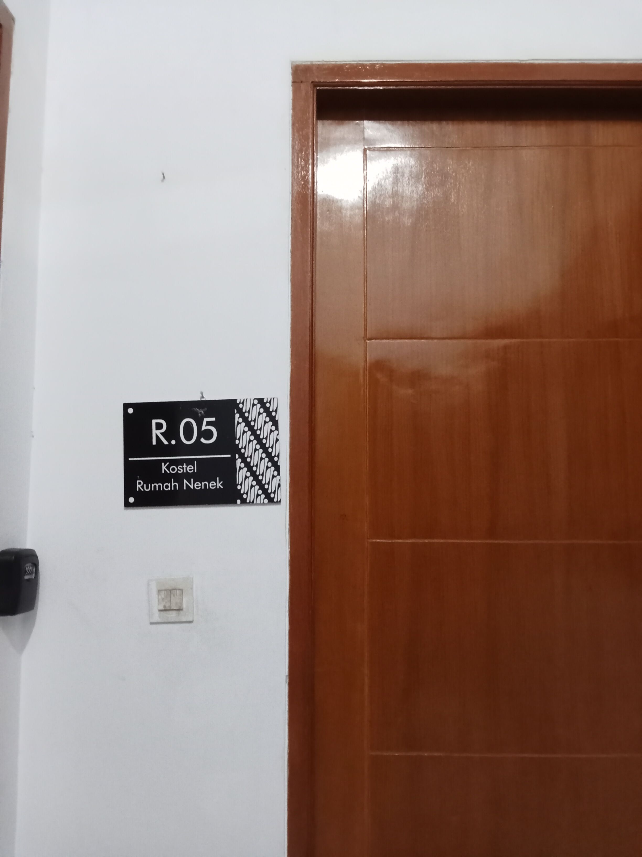 A door with a sign indicating room number R.05, a label for 'Kostel Rumah Nenek', and a light switch.