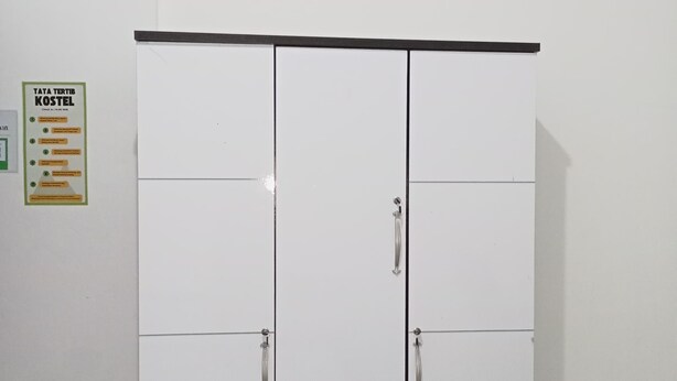 Ein weißer Kleiderschrank mit zwei Schubladen und zwei Türen, eine schwarze Oberseite und ein Schild an der linken Wand.