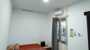 Ein schlichtes Zimmer mit zwei Betten, einem Fenster mit Vorhängen, einer Klimaanlage und einem Schild an der Wand.