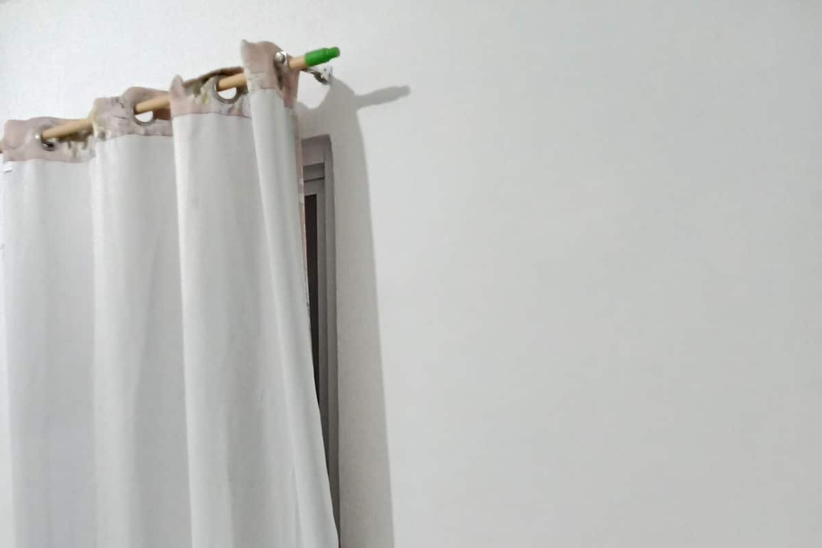 Een kamer met een wit gordijn, een zwarte stoel en een houten tafel.
