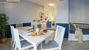 A dining area with a white table and chairs, a small kitchen in the background, and a blue and white color scheme. - Apartment with A/C and parking space | Ap12 (Imperia)