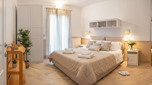 A bedroom with a large bed, bedside tables, a nightstand, a wooden chair, a potted plant, and a window with curtains. - Apartment with A/C and parking space | Ap12 (Imperia)