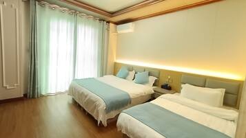 Habitación de hotel con dos camas, suelo de madera, ventilador de techo y una ventana grande con cortinas.