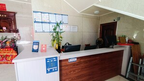 Un mostrador de recepción con detalles de madera, una planta y varios carteles informativos en la pared.