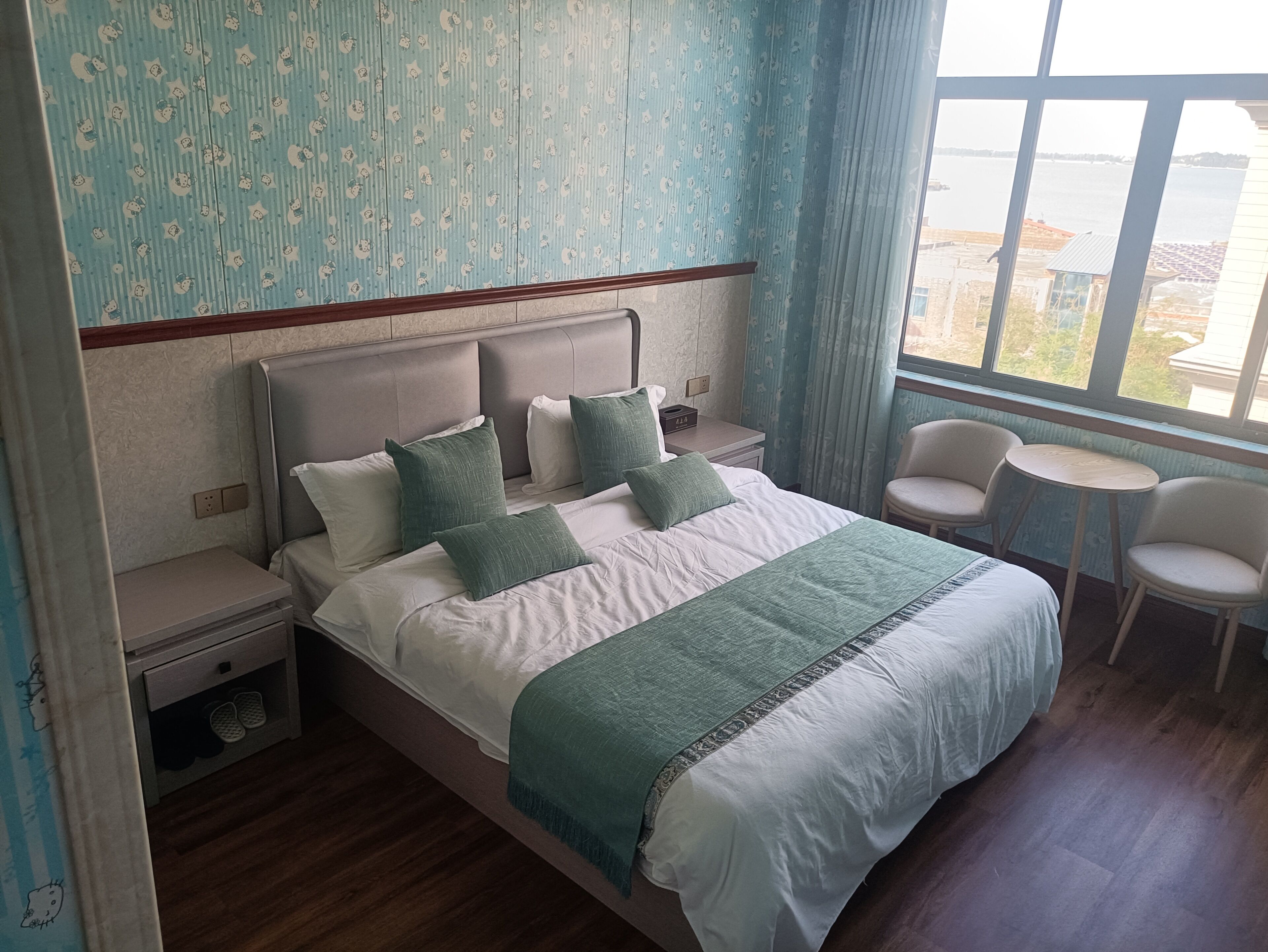 Un dormitorio ordenado con una cama grande, mesitas de noche, una silla y vistas al exterior.