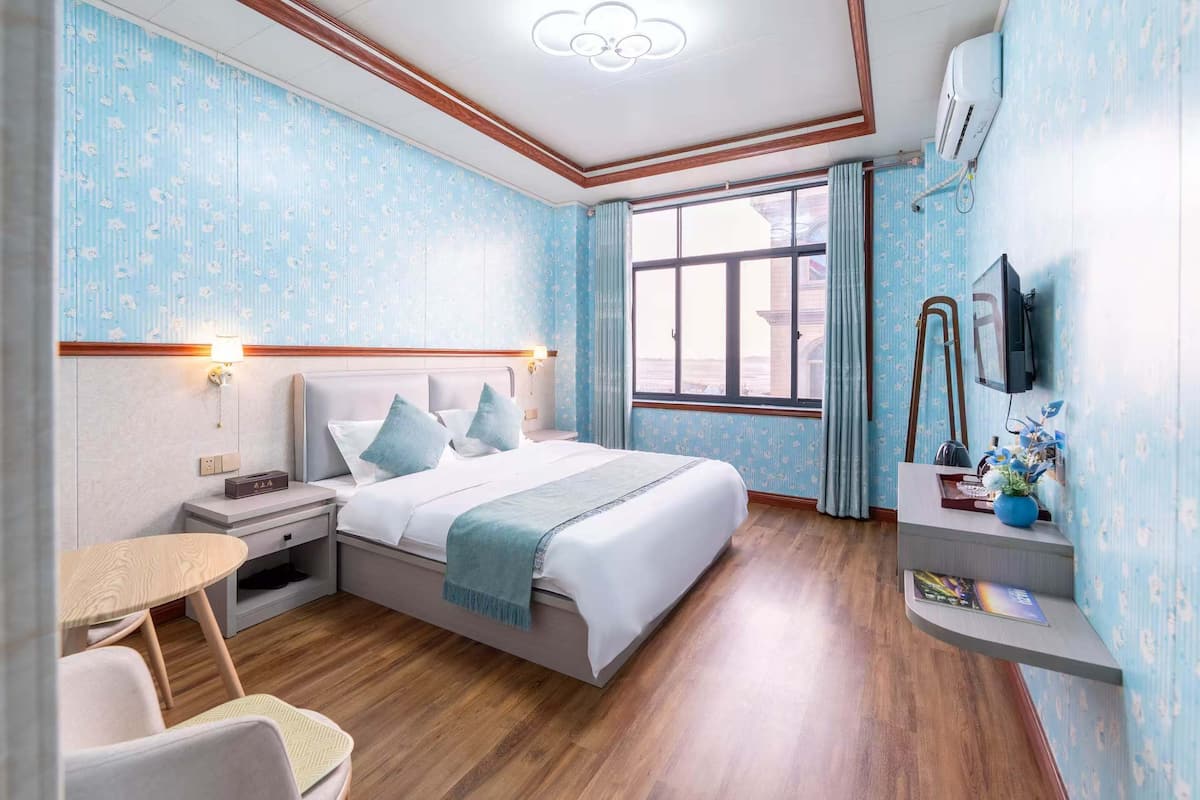 A hotel room with a bed, bedside table, chair, and a small desk with a lamp.