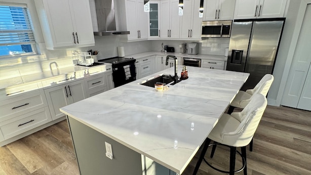 A modern kitchen with white cabinets, a large island with bar stools, stainless steel appliances, and pendant lighting. - Luxury, Brand NEW 4BR/3.5BA Townhome I South Tampa Gem I Central Location (Tampa)