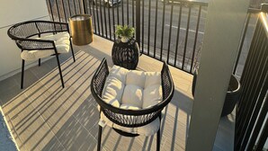 A balcony with two black wicker chairs and a small table, a potted plant, and a view of a parking lot and buildings in the background. - Luxury, Brand NEW 4BR/3.5BA Townhome I South Tampa Gem I Central Location (Tampa)