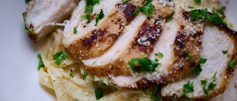 A plate of sliced grilled chicken breast over pasta, garnished with herbs.