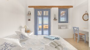 A bedroom with a bed, a desk, a chair, a window with a view, and a door. - Seaside 5BDR Bliss in Mykonos (Mikonos)