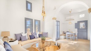 A modern living room with a sofa, a coffee table, and a dining area with chairs. - Seaside 5BDR Bliss in Mykonos (Mikonos)