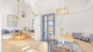 A modern living room with a sofa, a dining table, and a coffee table. There is a painting on the wall and a window with a view of the beach. - Seaside 5BDR Bliss in Mykonos (Mikonos)