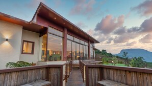 A modern building with large glass windows and a wooden deck. - Villa 27 Amarja's Mountain Crest (Mawal)