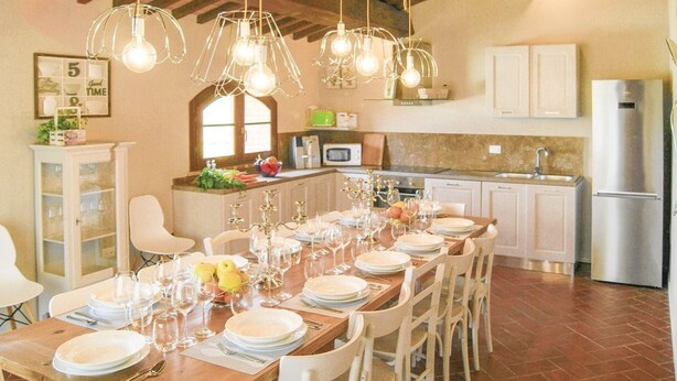 A dining area with a long wooden table set for a meal, surrounded by white chairs. - Ludovica and Marina Villas with 2 pools (Lajatico)