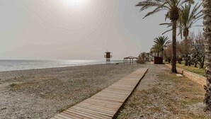 A beach with a wooden walkway, palm trees, and a lifeguard tower. - RentitSpain Castell Beach, Views, and Parking (Castell de Ferro)