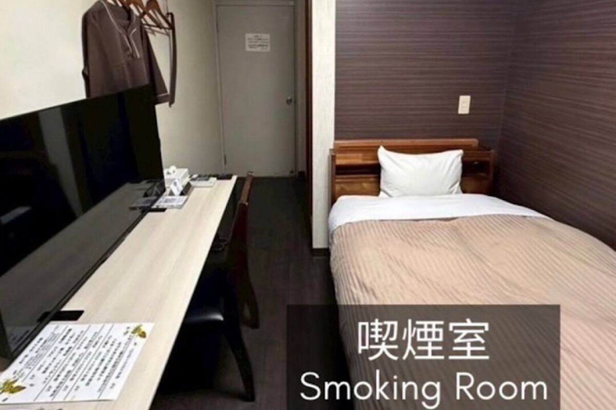 Habitación de hotel con cama, escritorio y televisor. Hay un cartel que indica que es para fumadores.