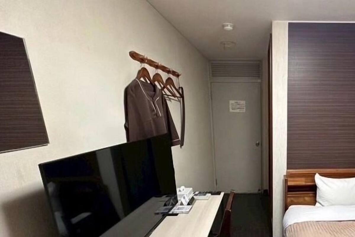 Habitación de hotel con cama, televisión, escritorio con silla y perchero con ganchos.