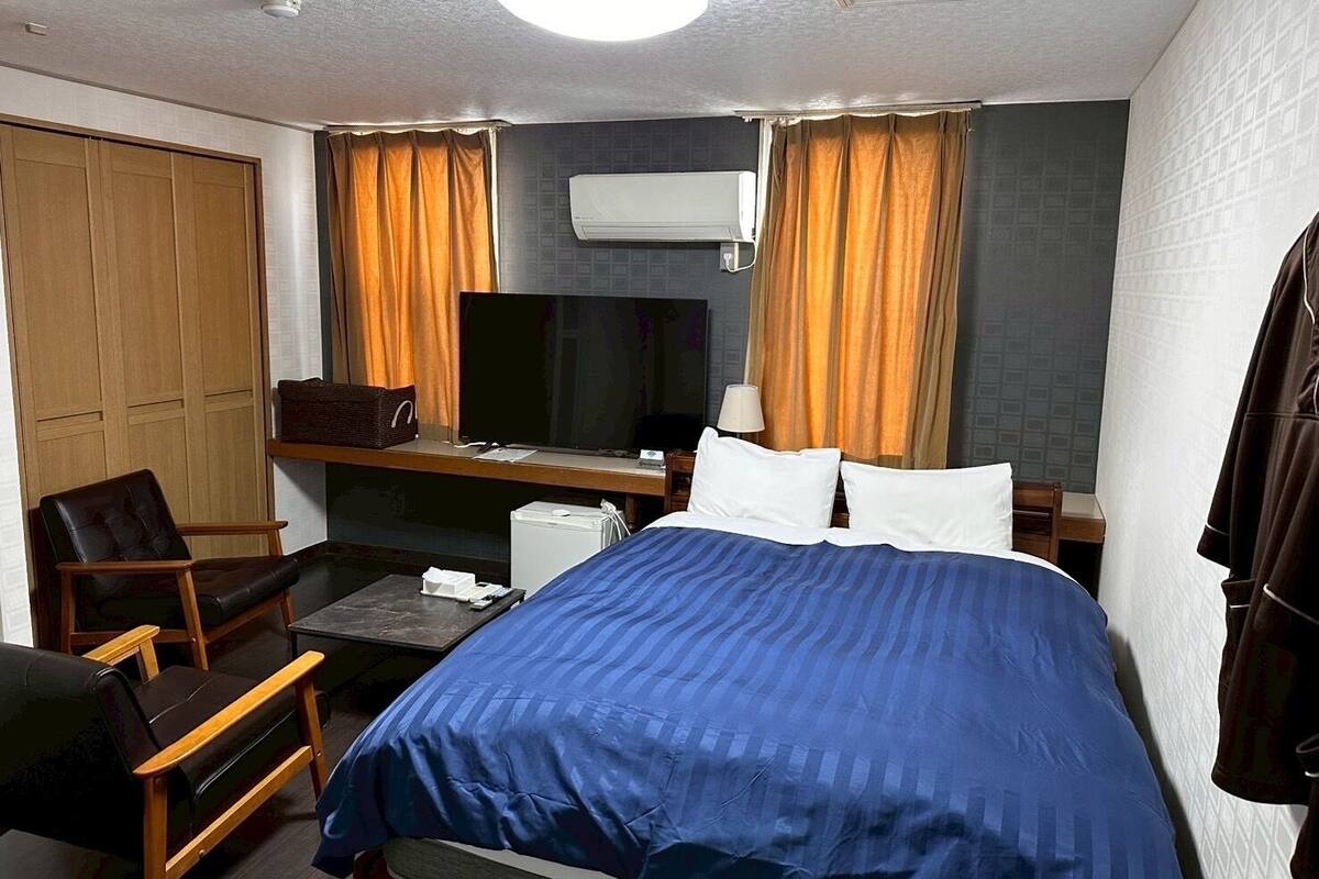 Una habitación de hotel con una cama, un escritorio, una silla, un equipo de aire acondicionado y cortinas.