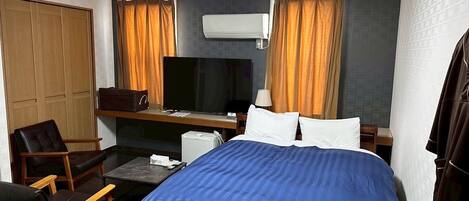Una habitación de hotel con una cama, un escritorio, una silla, un equipo de aire acondicionado y cortinas.