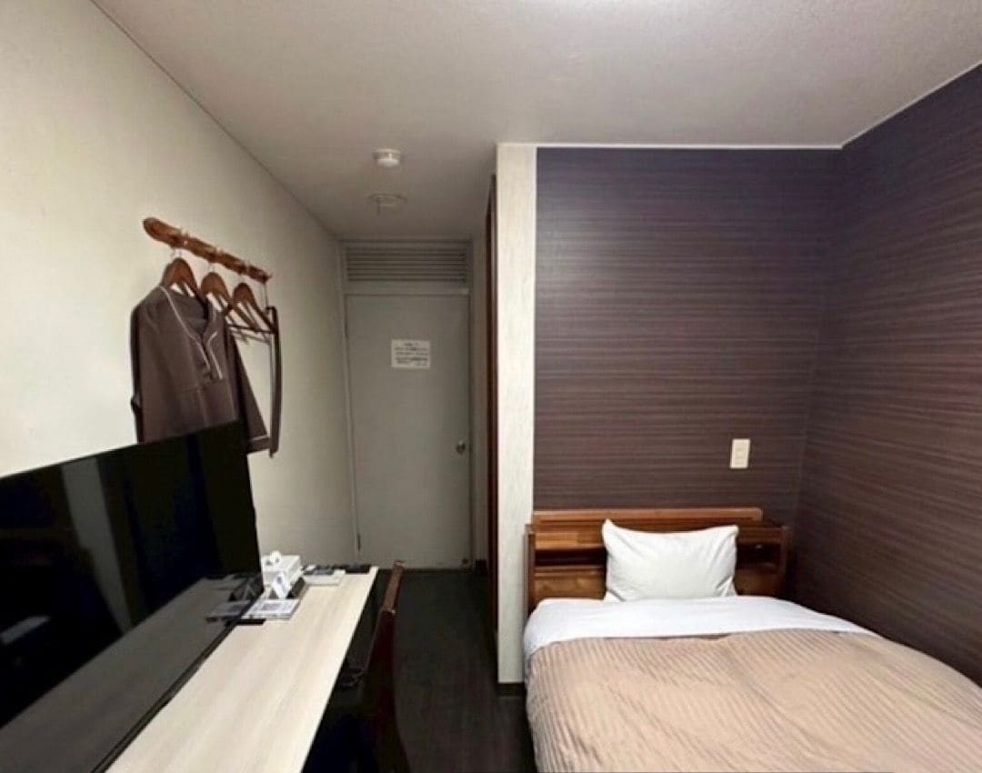 A hotel room with a bed, a desk, and a TV. There is a sign indicating it is a smoking room.