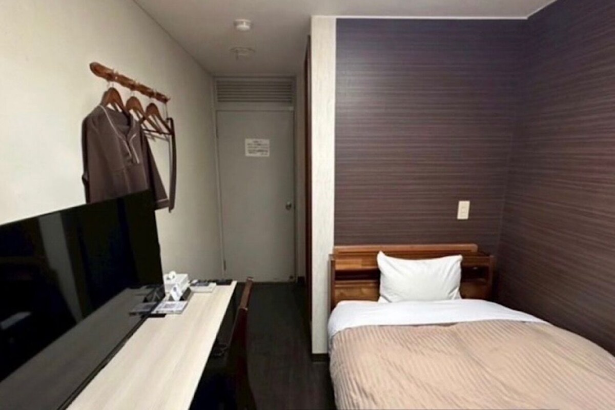 A hotel room with a bed, a desk, and a TV. There is a sign indicating it is a smoking room.