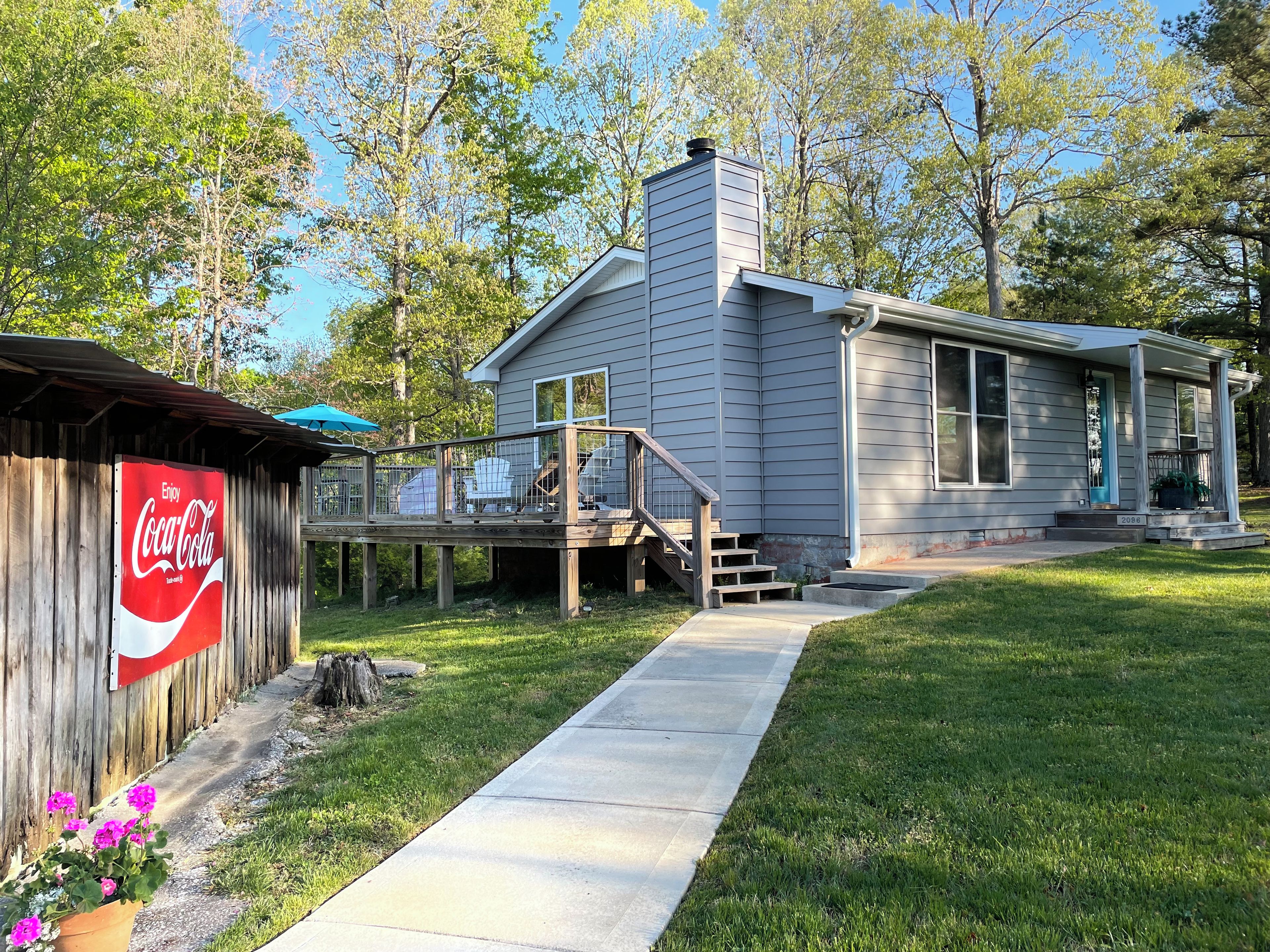 Une maison avec une terrasse, un panneau publicitaire Coca-Cola et une pelouse.