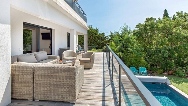 A modern outdoor deck with wicker furniture, a pool, and lush greenery. - Californian style pool villa for 10 people with air conditioning (ST AYGULF)