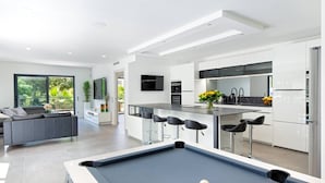 A modern kitchen with white cabinets, a central island with bar stools, a pool table, and a living area with a sofa and a TV. - Californian style pool villa for 10 people with air conditioning (ST AYGULF)