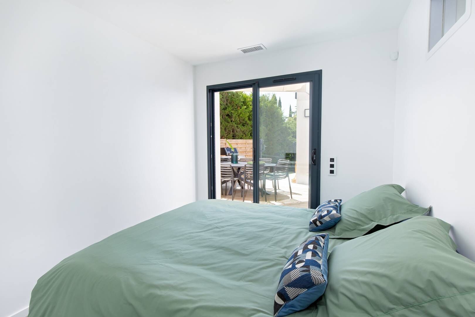 Un dormitorio con cama, una puerta corrediza de vidrio que da a un patio exterior con mesa y sillas.