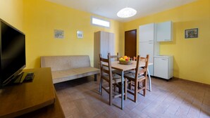 A compact living space with a sofa, a dining table with chairs, a television, and a refrigerator. - APPARTAMENTI LE PRADE - LE PRADE BILO 2 (Portoferraio)