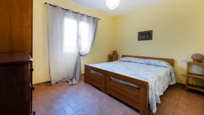 A bedroom with a wooden bed, a nightstand, a small table, and a wall-mounted shelf. - APPARTAMENTI LE PRADE - LE PRADE BILO 2 (Portoferraio)