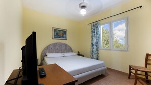 A bedroom with a bed, a desk with a television and remote, a chair, a window with curtains, and a ceiling fan. - APPARTAMENTI LE PRADE - LE PRADE BILO 5 (Portoferraio)