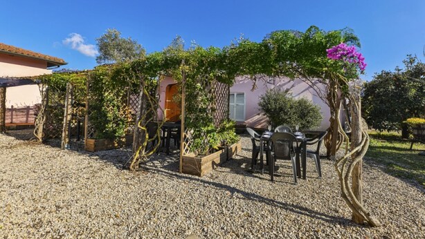 A patio area with a pergola, outdoor seating, and a building in the background. - APPARTAMENTI LE PRADE - LE PRADE BILO 5 (Portoferraio)